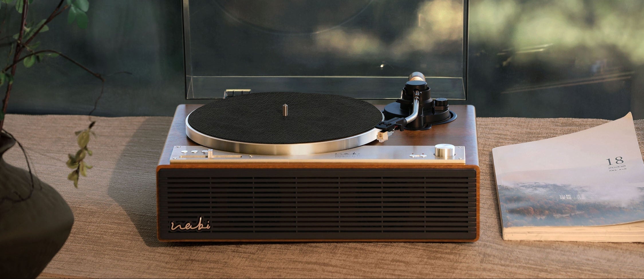 建议的替代文本 (Alt Text)
Front view of the Tinyl WABI all-in-one record player featuring a minimalist wood-grain finish and a premium metal speaker grille. Set in a peaceful, sunlit environment to highlight the high-power 100W speaker system and zen-inspired wabi-sabi design for modern home audio.